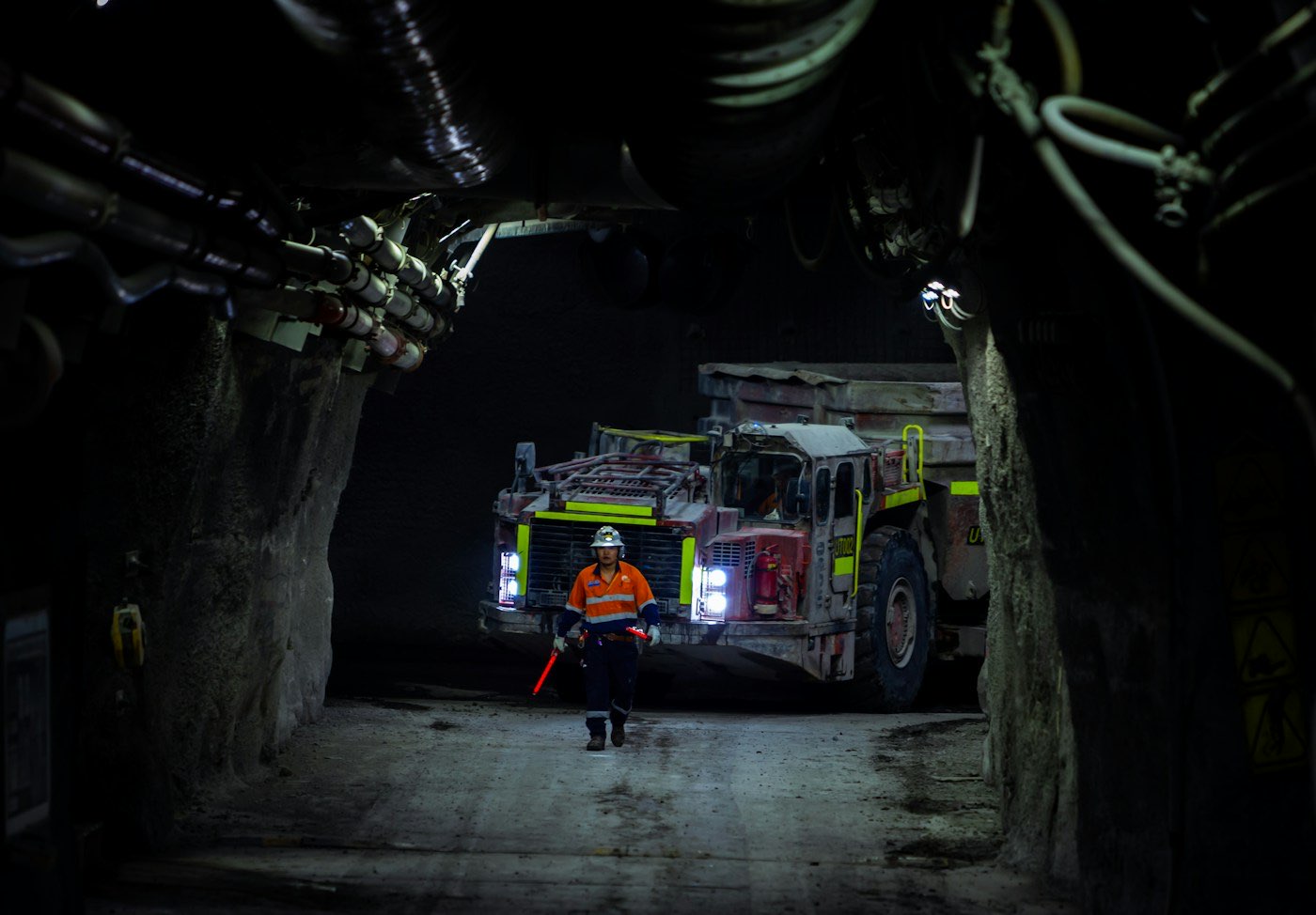 Miner in an underground tunnel beside a lit mining vehicle